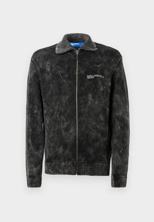 Melna korduroja jaka ar ribotu tekstūru, stāvošu apkakli un priekšējo rāvējslēdzēju; uz krūtīm ir 'Karl Lagerfeld Jeans' logo.