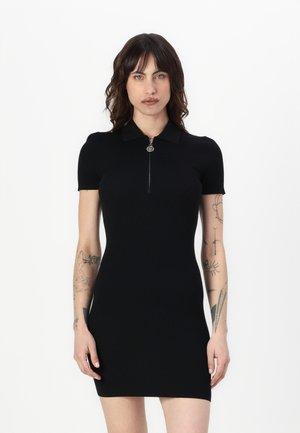 Robe noire à manches courtes avec un col zippé, texture côtelée, forme ajustée et détail subtil en métal argenté au niveau du zip.
