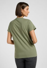 Olive zielona bawełniana koszulka z krótkim rękawem i okrągłym dekoltem, charakteryzująca się gładką teksturą i luźnym krojem. Minimalistyczny design.