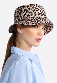 Leopardenmuster-Bucket Hat aus Stoff, mit breiter Krempe und gesticktem Logo. Weiche Textur in Beige- und Schwarztönen.