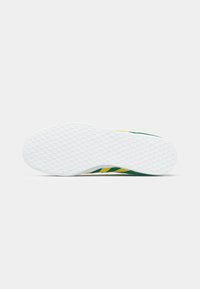 Πράσινη και κίτρινη σόλα αθλητικού παπουτσιού με υφή λευκού καουτσούκ, που διαθέτει μοτίβο κυψέλης και διαγώνιες ρίγες σε πράσινο και κίτρινο.