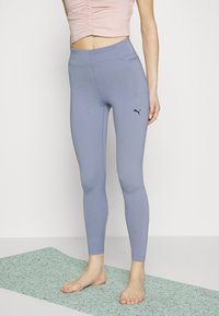 Jasnoniebieskie legginsy z elastycznego materiału z wysokim stanem i czarnym logo Pumy na dolnej części lewej nogawki, w zestawie z różowym topem na krótko.