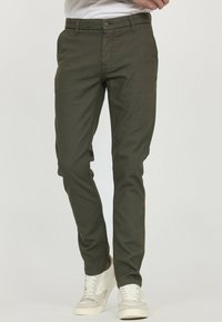 Pantalon vert olive à coupe slim, doté d'un tissu texturé, de passants de ceinture et de poches avant. Associé à des baskets beiges.