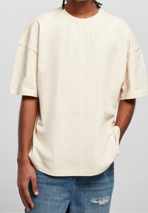 T-shirt beige oversize avec manches courtes et col rond, en coton doux, avec une poche latérale et une coupe décontractée.