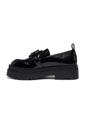 Black patent leather shoe with a chunky rubber sole, featuring a decorative strap and metal accents, designed for a sleek, modern look.