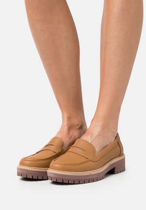 Mocassins en cuir tan avec un bout arrondi, présentant des coutures décoratives et une semelle épaisse et crantée pour l'adhérence et le confort.