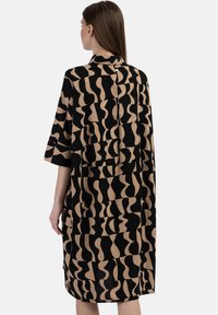 Fließendes schwarzes und beiges Kleid mit abstrakten wellenförmigen Mustern, kurzen Ärmeln, hohem Ausschnitt und einem Knopfverschluss hinten. Glatte Stofftextur.