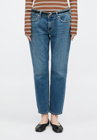 Hele sinised sirgelõikelised teksad, millel on viis taskut, õrn pleekimine ja õmbluse detailid. Kandmisega pruunikirju pika varrukaga pluus ja mustad madalad kingad.