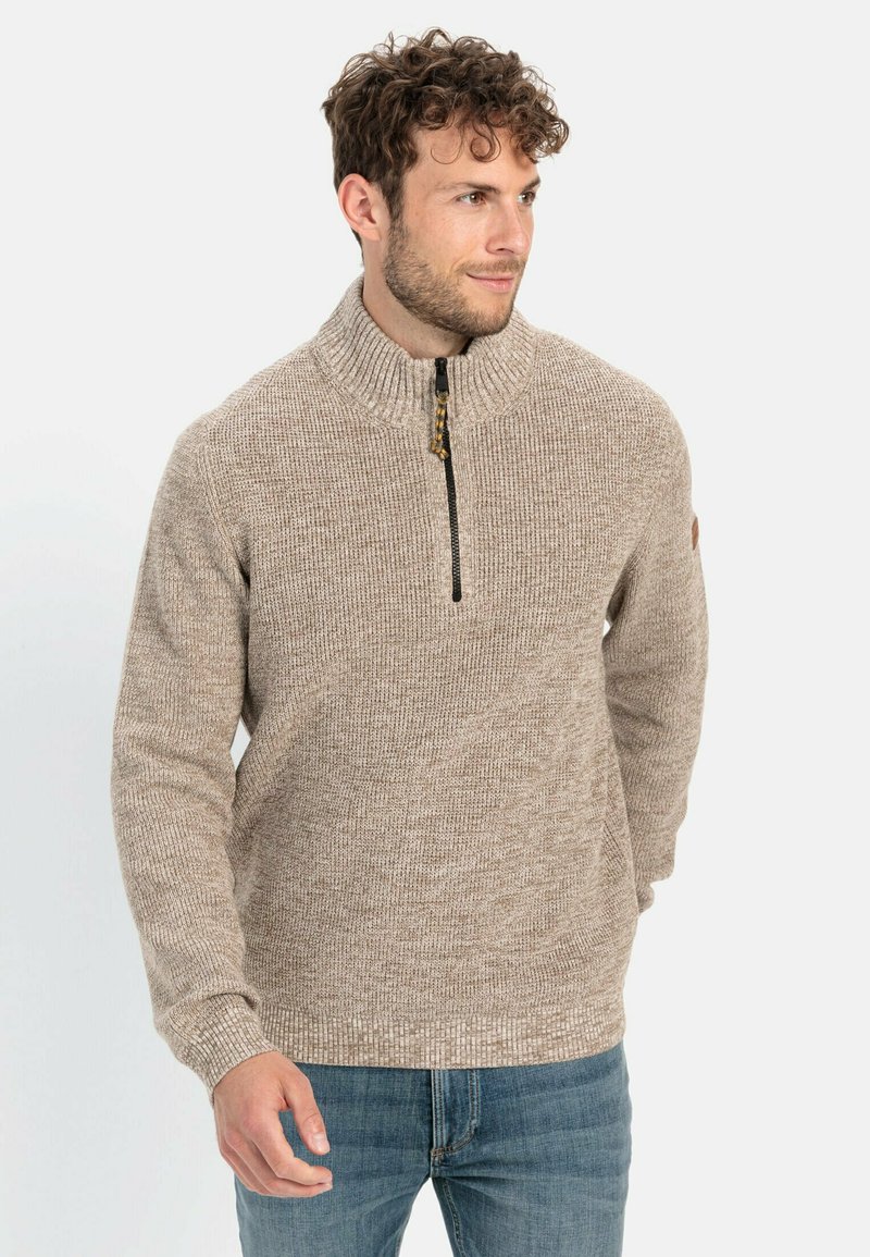Beige trui met een hoge kraag en een halve rits aan de voorkant, met een gestructureerd gebreid patroon, geribbelde manchetten en een klein logo-opdruk op de linkermouw.