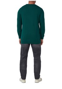 Türkiser langärmliger Strickpullover mit Rundhalsausschnitt, kombiniert mit grauen Jeans und weißen Sneakers, zeigt eine solide Textur und einen lockeren Schnitt.