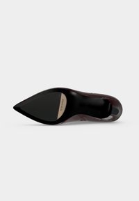 Chaussure à talon haut bordeaux vue par le dessous montrant un bout pointu et une semelle noire avec étiquette de marque "Peter Kaiser."