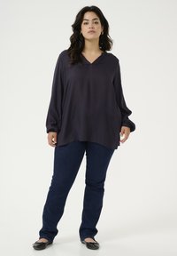 Dark purple long-sleeve top with a v-neck and subtle gathering at the wrists, paired with dark blue straight-leg jeans and black flats.