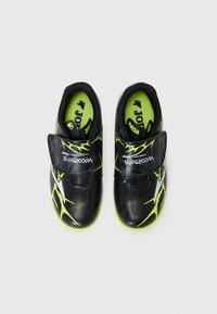 Scarpe da calcio nere con dettagli verdi, dotate di una cinghia in velcro e una parte superiore testurizzata con un design grafico accattivante. Soletta imbottita visibile.