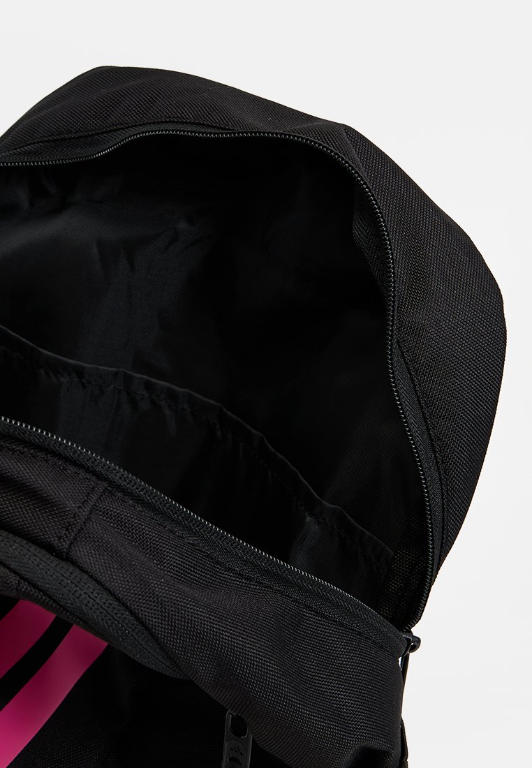 Mochila negra con exterior texturizado y un detalle en rosa. La cremallera superior revela un interior espacioso de tela negra con correas elásticas.
