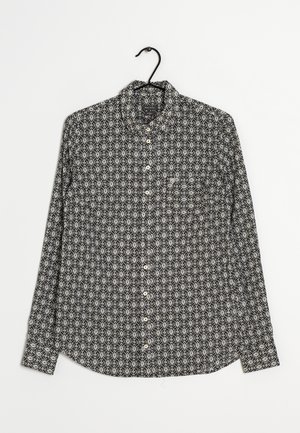 Chemise à manches longues en noir et blanc présentant des motifs géométriques complexes, un col boutonné et une poche poitrine. Tissu en coton, texture lisse.