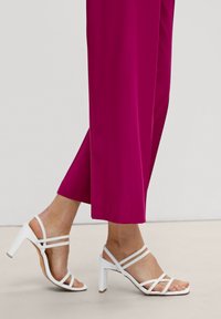 Fuksjowe spodnie szerokie w nogawkach, połączone z białymi sandałami na wysokim obcasie z paskami. Skup się na gładkiej tkaninie i eleganckim designie butów.