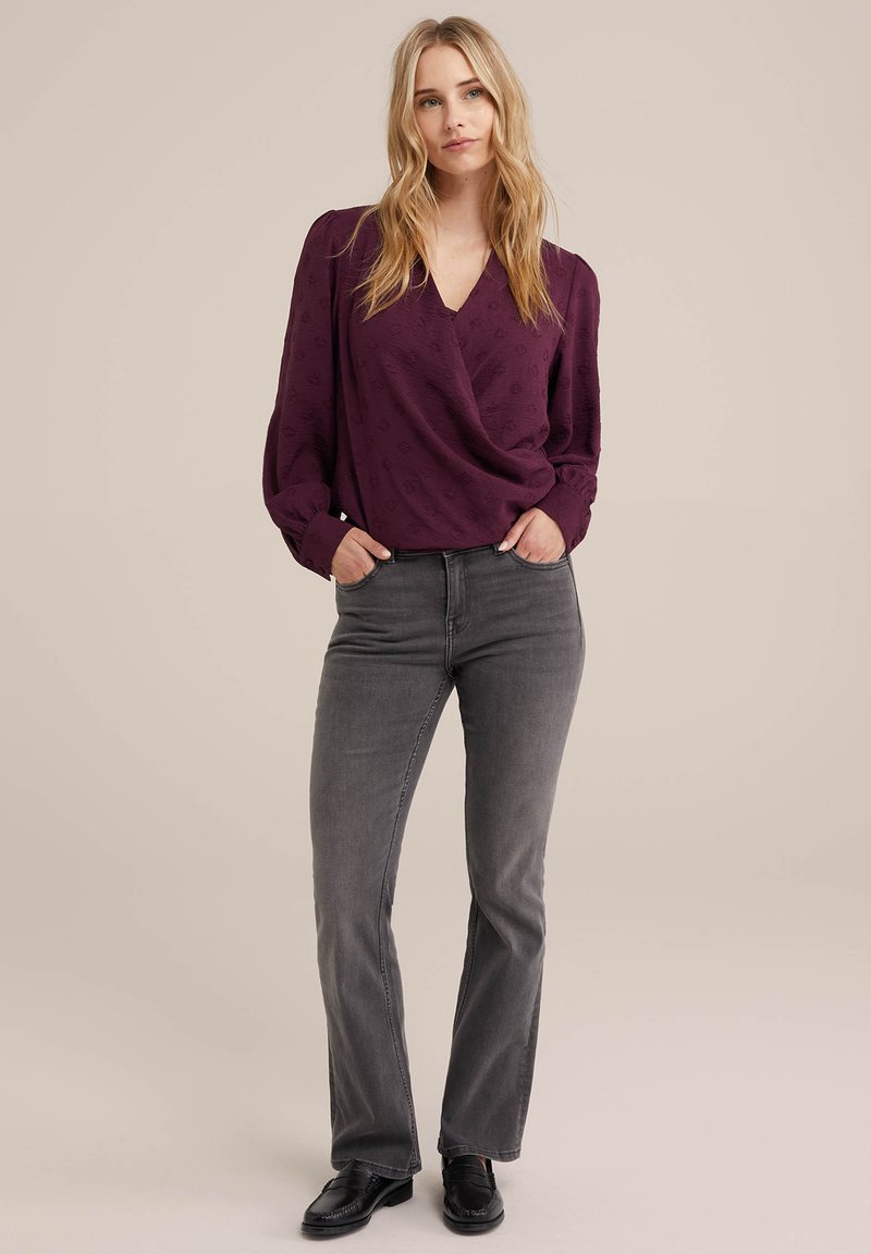 Paarse blouse met een wikkelontwerp en subtiel patroon, gecombineerd met grijze flare jeans en zwarte instappers. Glad materiaal en lange mouwen.