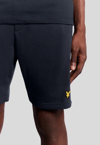 Donker marineblauwe sportshorts van een lichtgewicht stof, met een gele geborduurde logo aan de onderrand en een gladde textuur.