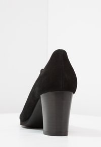 Svart mocka högklackad sko med rund tå och kraftig klack, med en mjuk textur och enkla design detaljer.