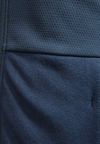 Marineblaues Gewebe mit zwei Texturen: einem glatten, gewebten Abschnitt mit einem erhabenen Muster oben und einem weichen, flauschigen Fleece unten.