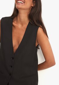 Must mustrühmatu must vest, millel on sügav V-kaelus, kolm nööpi ja kaks esikotti, kohandatud sobivus, sile tekstuur.