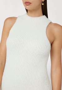 Top senza maniche a coste bianche con un collo alto, realizzato in materiale morbido e testurizzato. Presenta una silhouette aderente con dettagli delicati.