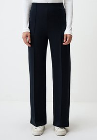 Pantalons noirs taille haute, ajustés, avec une coupe �évasée, dotés de plis à l'avant et d'un tissu lisse. Accentués par une finition soignée.