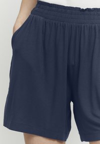 Shorts bleu marine avec taille élastique et poches latérales, fabriqués dans un tissu doux et léger. Caractérisés par une coupe décontractée et des ourlets finis.