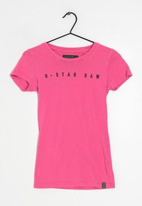 Růžové bavlněné tričko s krátkým rukávem, se zaobleným výstřihem a černým textem "G-STAR RAW" tištěným na přední straně. Viditelný štítek velikost S.