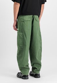 Zöld cargo nadrág laza szabással, több zsebbel és puha textúrával. Fekete sportcipővel viselve.