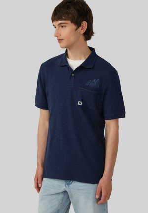 Polo navy hecho de tejido suave, con una tapeta de tres botones, un bolsillo de parche con un diseño gráfico azul y mangas cortas.