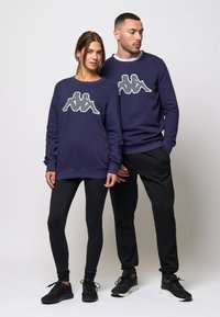 Námornícke mikiny s logom Kappa, v kombinácii s čiernymi legínami a teniskami. Hladká tkanina, okrúhly výstrih a elastické manžety.