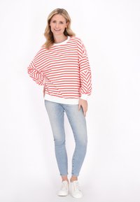 Rood-wit gestreepte sweatshirt met een brede pasvorm, ballonmouwen en een witte ribbelzoom, gedragen met lichtblauwe skinny jeans en witte sneakers.