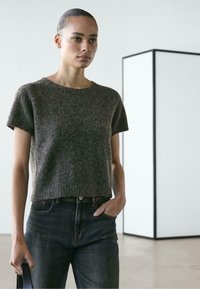 Brązowy sweter z krótkim rękawem wykonany z miękkiego, teksturowanego dzianiny. W połączeniu z ciemnymi dżinsami, strój cechuje się luźnym krojem i prostym designem.