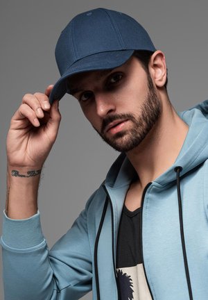Blue baseball cap with a curved visor, combined with a light blue zip-up hoodie. The fabric appears smooth, with visible stitching details.