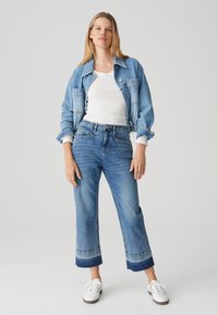 Denimjack en cropped jeans in lichtblauw, met een knoopsluiting en contrasterende zoom. Witte langemouwen shirt en witte sneakers.