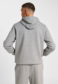 Szara, kapturowa bluza z miękką teksturą, luźnym krojem i kieszenią kangurką. Ubranie ma prosty, nieozdobiony design.