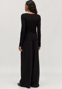 Schwarzes Langarmshirt mit taillierter Passform, kombiniert mit weit geschnittenen schwarzen Hosen. Glattes Material mit einem leichten Glanz, keine sichtbaren Muster oder Akzente.