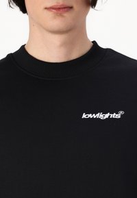 Sort sweatshirt med ribbede rund halsudskæring og et hvidt broderet "lowlights" logo på venstre side. Glat stofstruktur.