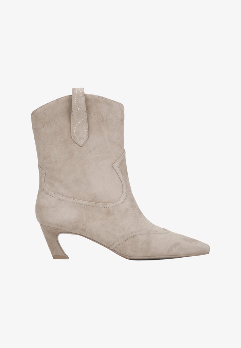 Bottine en suede beige, à bout pointu, avec un côté texturé et un petit talon évasé. Présente des coutures décoratives et une languette.