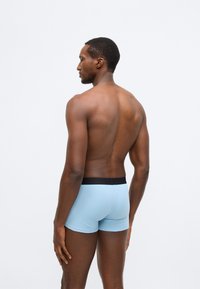 Ανοιχτό μπλε μποξεράκια με μαύρη ελαστική ζώνη στη μέση, εμφανιζόμενα από πίσω, που αναδεικνύουν την ομαλή υφή και το εφαρμοστό σχέδιο.