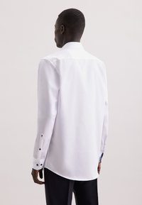 Witte lange mouwen shirt met een klassieke kraag, gladde textuur, afgeronde zoom en zwarte knoopaccenten op de manchetten. Eenvoudig en chic ontwerp.