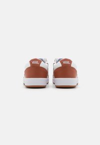 Vans sko i hvit og brun syntetisk skinn, lågt design, flat hvit gummisåle og signaturlogo på baksiden av hælen.
