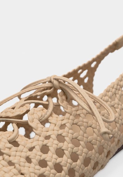 Μπεζ υφασμένο επίπεδο παπούτσι με περίπλοκο πλεγμένο σχέδιο λαβύρινθου και δεμένη λεπτομέρεια φιόγκου στην κορυφή.