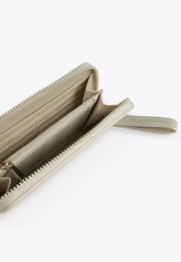 Cartera beis con cremallera, exterior texturizado, múltiples ranuras para tarjetas, un compartimento central y forro de tela. La tira de la cremallera incluye un detalle del logo.