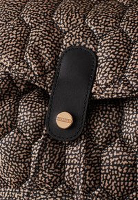 Quilted handbag featuring a hexagonal pattern in tan and black, with a black leather strap and a gold-tone snap closure detail.