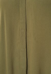 Tissu vert olive avec une surface douce et texturée. Présente une couture centrale verticale, créant un design simple mais épuré.