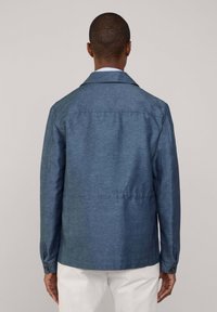 Ciemnoniebieska, teksturowana kurtka z kołnierzem, długimi rękawami i zapięciem na guziki przy mankietach. Tył ma prosty krój, a tkanina ma delikatny połysk.