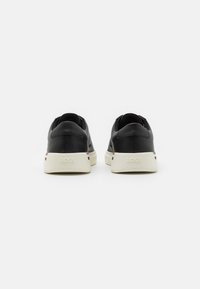 Svarta låga sneakers med ovandel i texturerad läder, kontrasterande vit gummisula och logodetaljer på hälen. Minimalistisk design.
