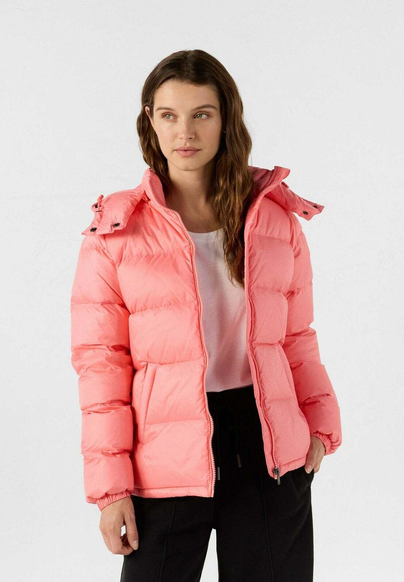 Roze pufferjack met een gewatteerd ontwerp, hoge kraag en ritssluiting aan de voorkant. Voorzien van elastische manchetten en twee zijzakken. Lichtgewicht en gewatteerd.